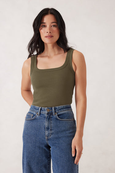 Woman wearing a green tank top and blue jeans against a white background